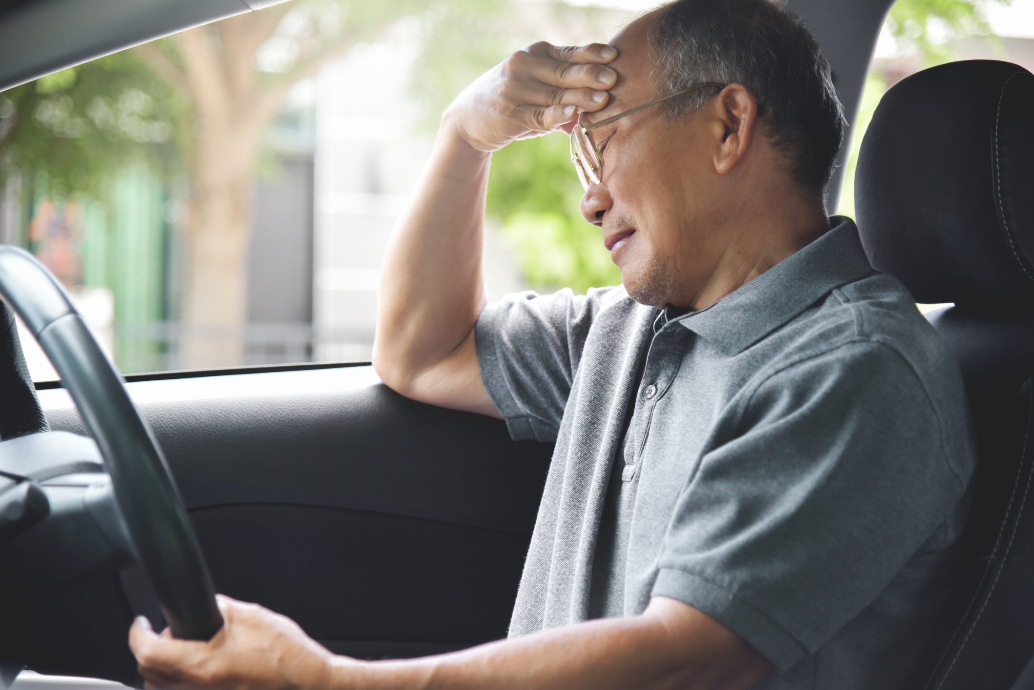 Asian Senior man having headache from migraine while driving a car. Illness, exhausted, disease.